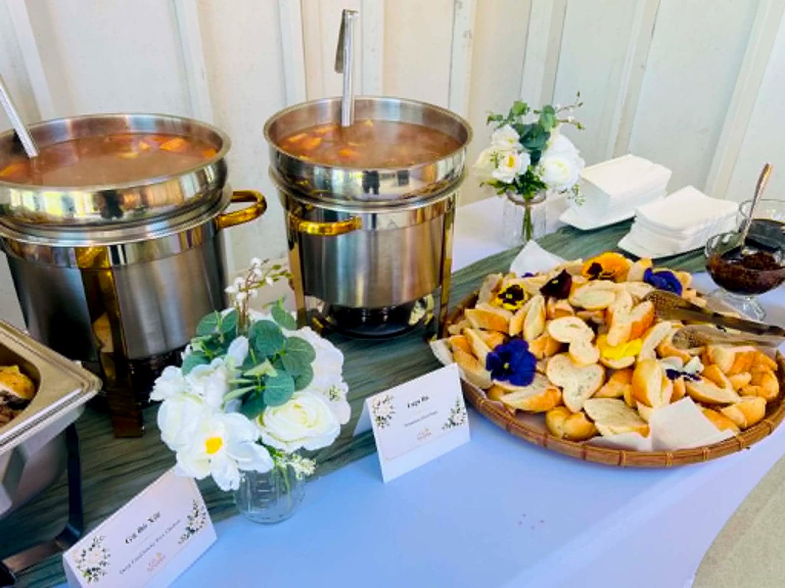 Buffet table with two soup warmers, a basket of bread and white floral centerpieces