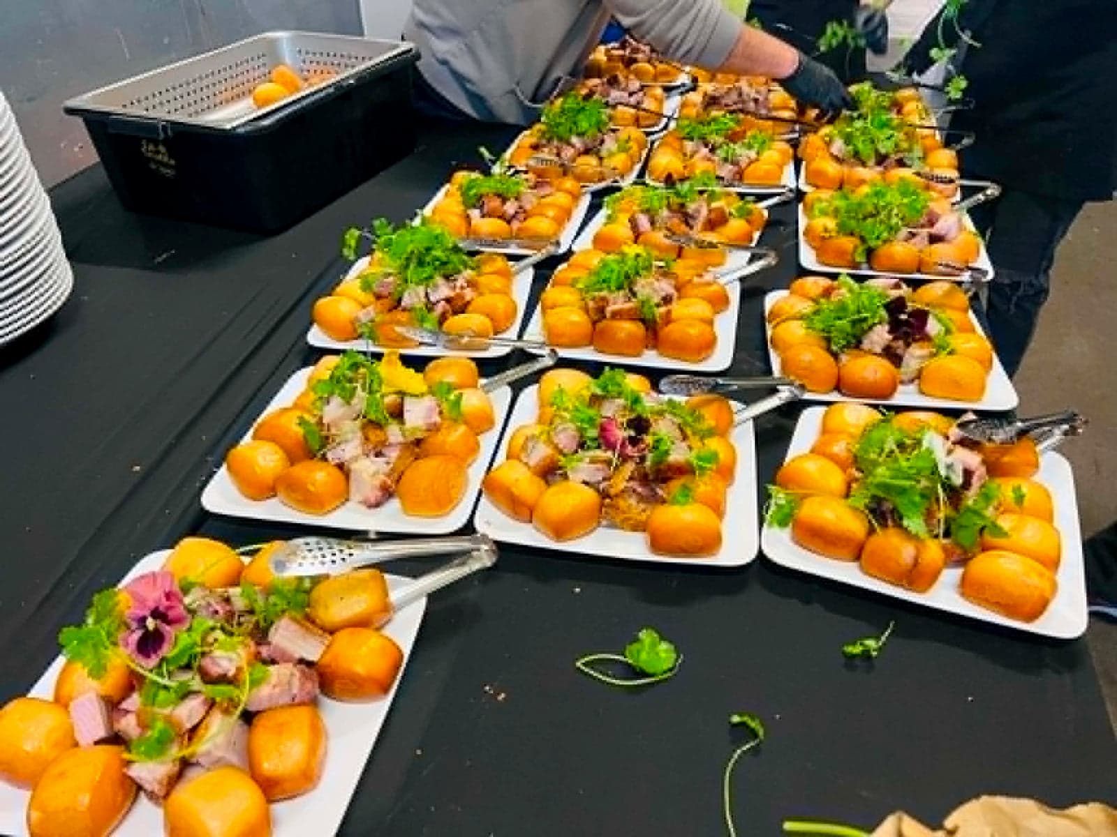 Plates of fried buns topped with sliced meat and herbs on a black table